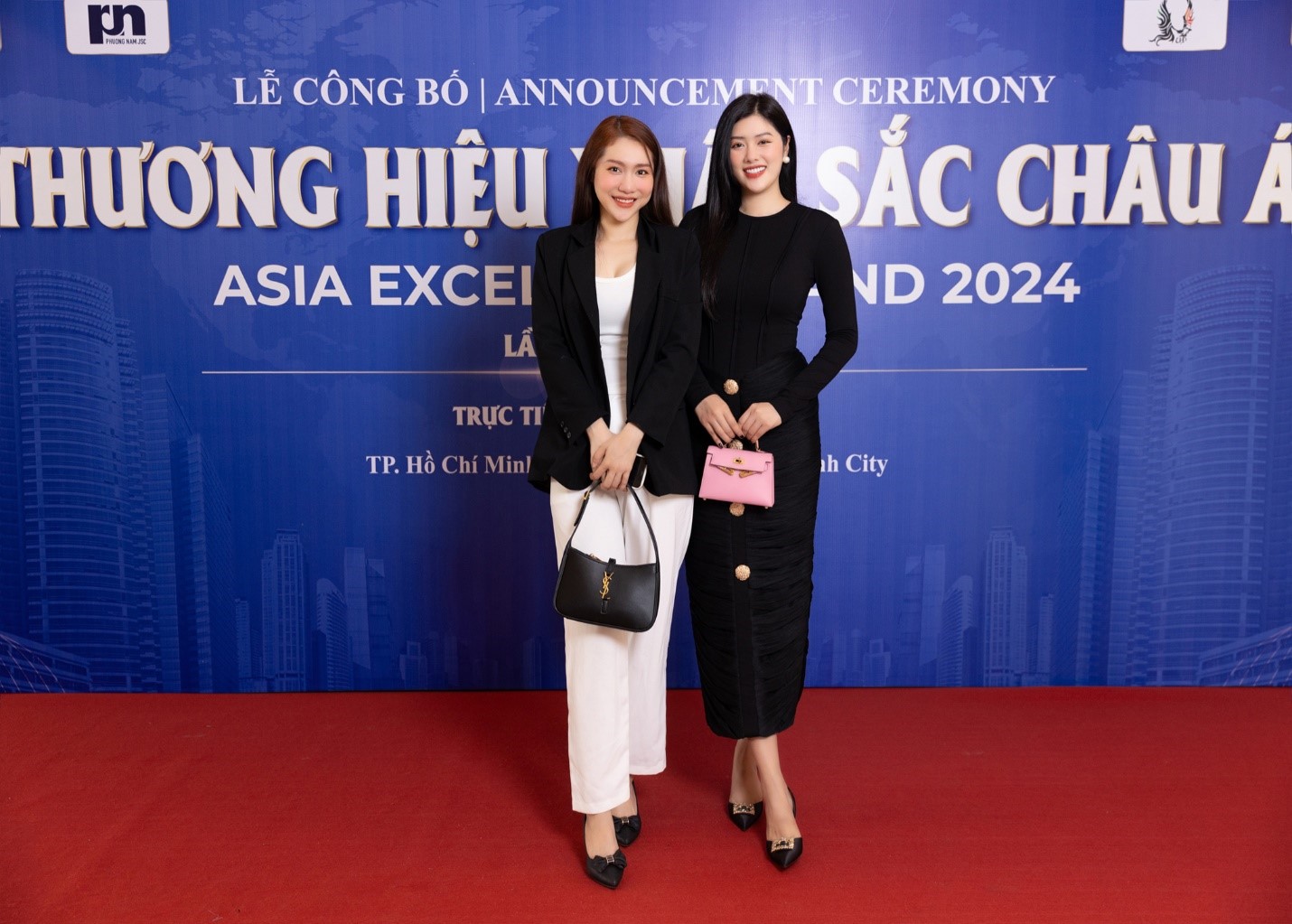 Two women standing in front of a blue signDescription automatically generated